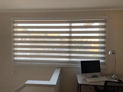 Roller duo con franjas alternadas regulando la luz sobre un escritorio junto a la ventana
