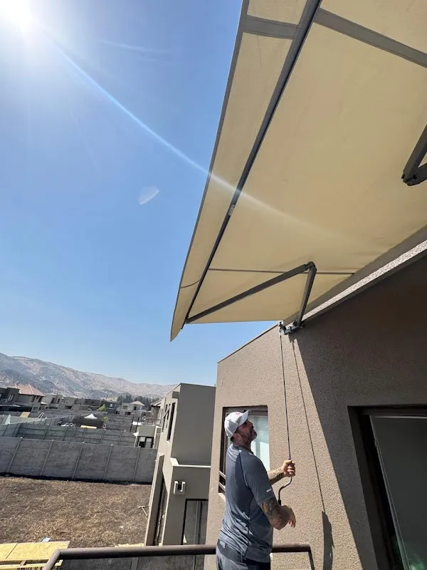 Toldo proyectante extendido desde el muro de una terraza, accionado a manivela un día de sol