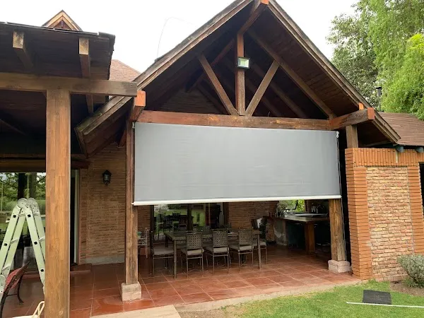 Toldo vertical bajado sobre el frente de un quincho, cerrando el comedor exterior del sol